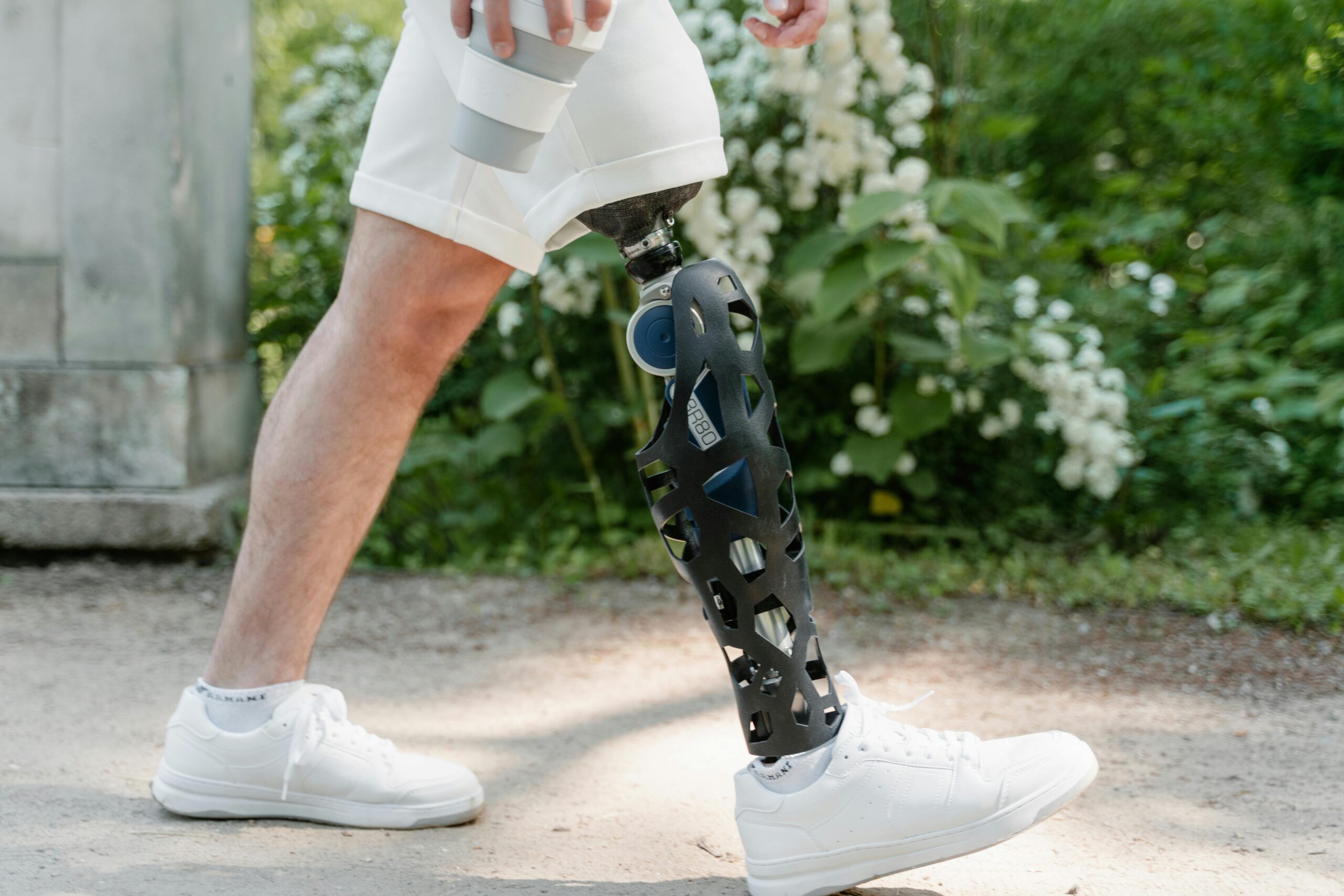 A close-up view of an adult male walking with a prosthetic leg and wearing sneakers outdoors.